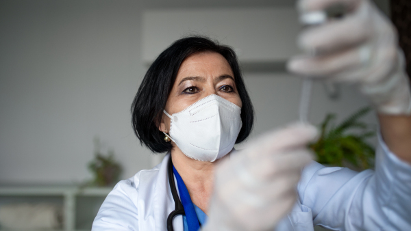 A portrait of senior woman doctor with syringe standing in hospital, coronavirus concept.