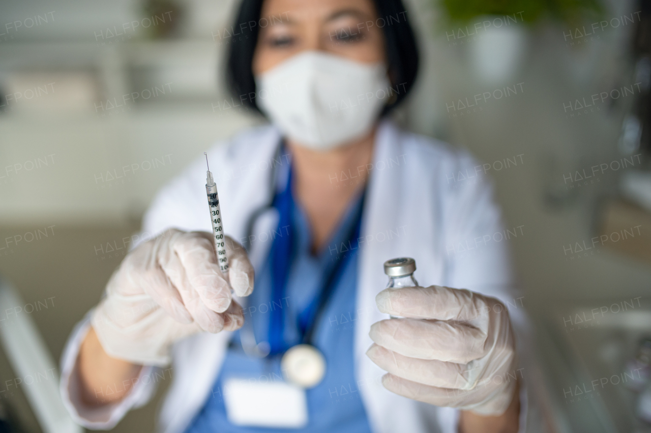 A portrait of senior woman doctor with syringe standing in hospital, coronavirus concept.