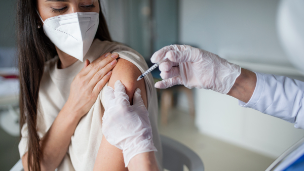 Mid adult woman with respirator getting vaccinated in hospital, coronavirus and vaccination concept.