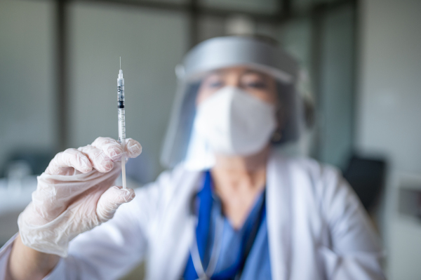 A portrait of senior woman doctor with syringe standing in hospital, coronavirus concept.