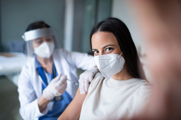 Happy woman with face mask getting vaccinated and taking selfie in hospital, coronavirus and vaccination concept.