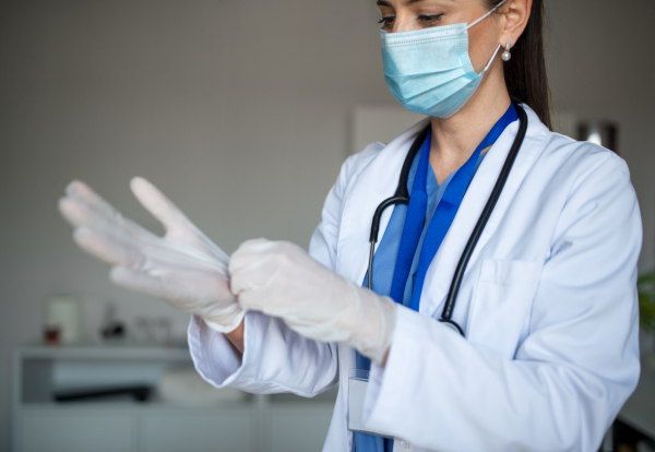 A portrait of woman doctor putting on gloves in hospital, coronavirus concept.