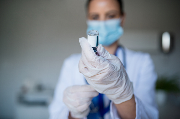 A portrait of woman doctor with syringe standing in hospital, coronavirus concept.