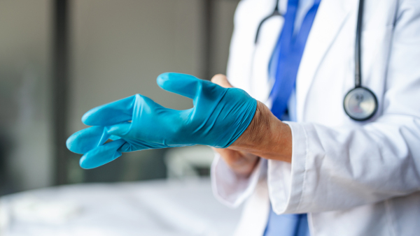 Midsection of unrecognizable senior woman doctor putting on gloves in hospital, coronavirus concept.