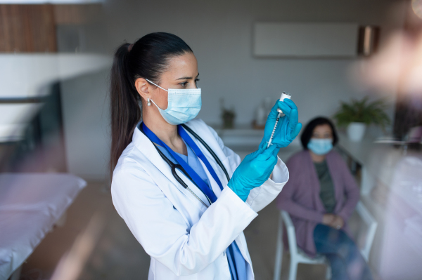 A portrait of woman doctor with syringe standing in hospital, coronavirus concept.