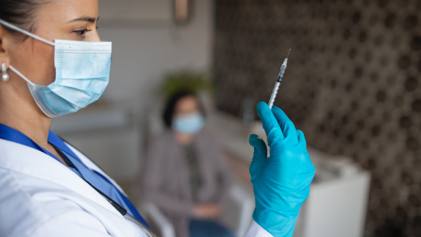 A portrait of woman doctor with syringe standing in hospital, coronavirus concept.