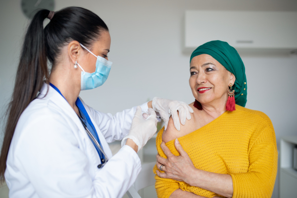 Happy woman with smartphone getting vaccinated in hospital, coronavirus and vaccination concept.