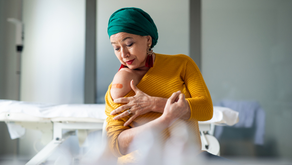 Happy senior woman with head wrap showing arm after vaccination in hospital, promotion concept.