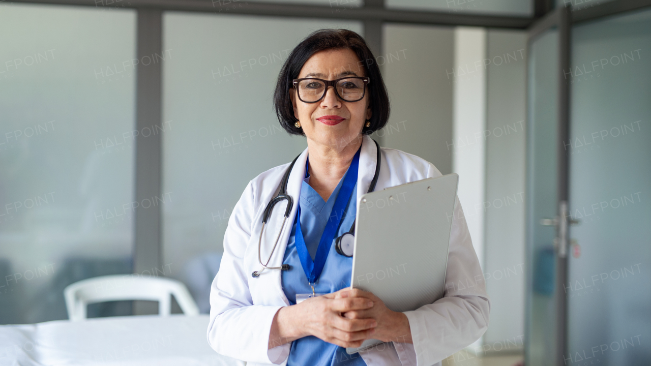 Front view portrait of senior woman doctor standing in hospital, looking at camera.