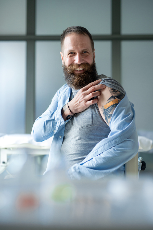 Portrait of happy man with plaster on arm after vaccination in hospital, looking at camera.