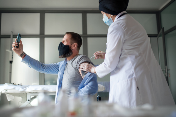 Mature man taking selfie when getting vacinated, coronavirus and vaccination concept.