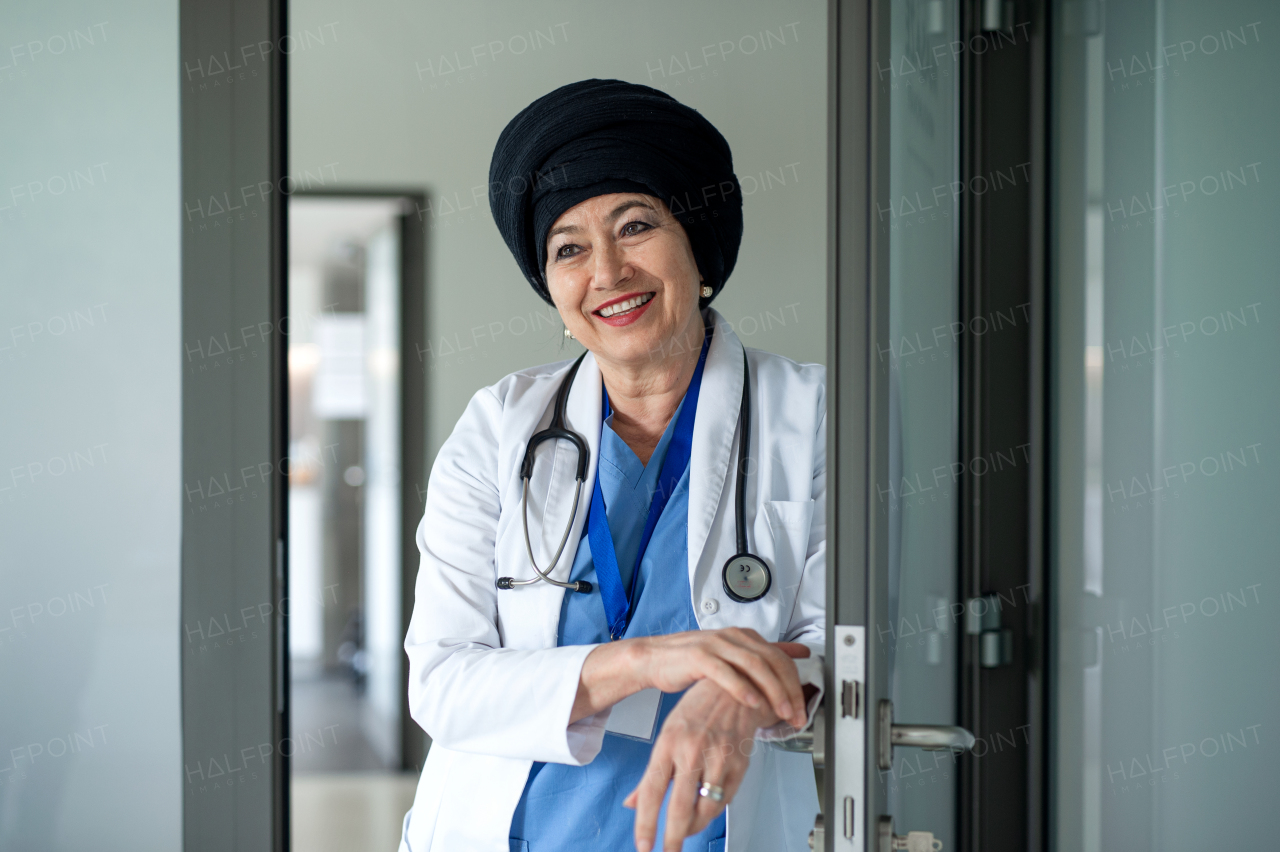 Front view portrait of senior woman doctor standing in hospital, looking at camera.