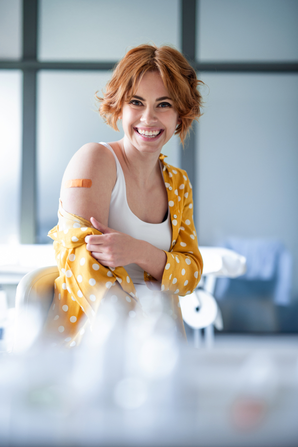 Portrait of happy woman with plaster on arm after vaccination in hospital, looking at camera.