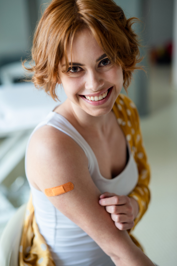 Portrait of happy woman with plaster on arm after vaccination in hospital, looking at camera.