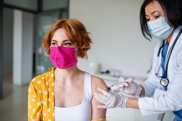 Portrait of young woman with face mask getting vaccinated in hospital, coronavirus and vaccination concept.