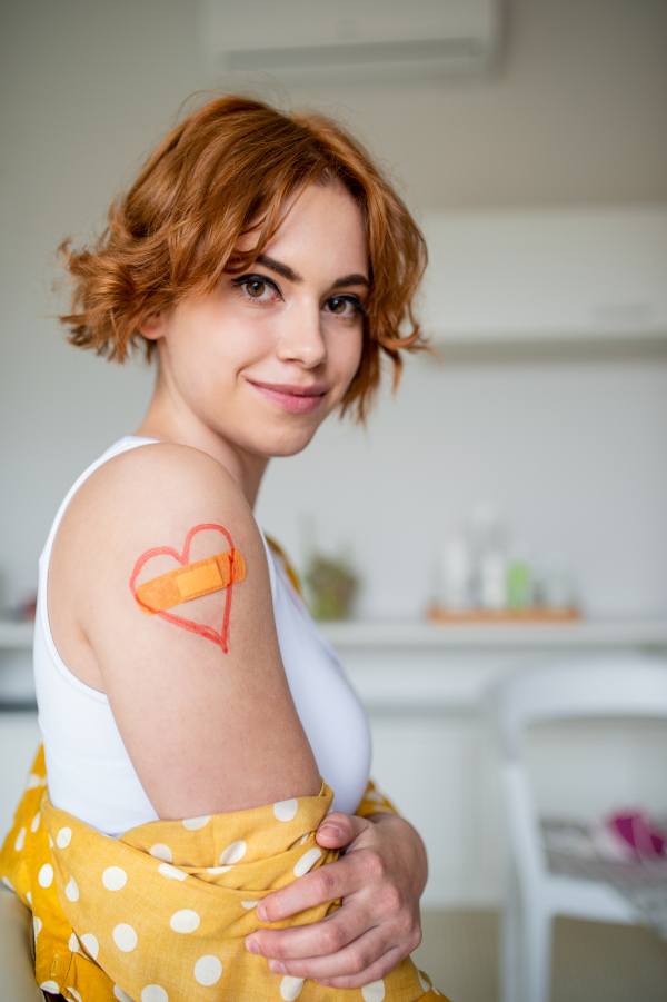 Portrait of happy woman with plaster on arm after vaccination in hospital, looking at camera.