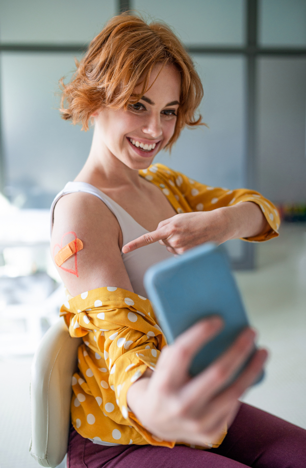 Portrait of happy woman with plaster on arm after vaccination in hospital, taking selfie.