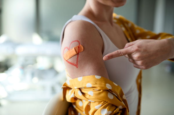 Unrecognizable young woman with plaster on arm after vaccination in hospital, promotion concept.