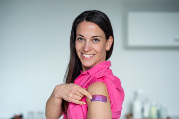 Portrait of happy woman with plaster on arm after vaccination in hospital, looking at camera.