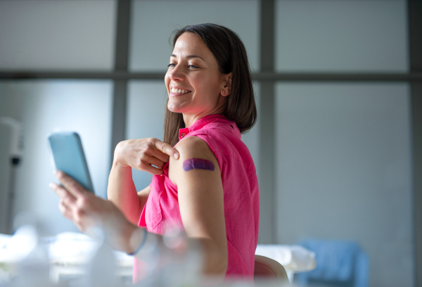 Portrait of happy woman with plaster on arm after vaccination in hospital, taking selfie.