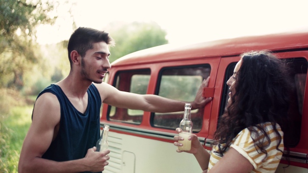 A young couple with bottles of drink on a roadtrip through countryside, talking.