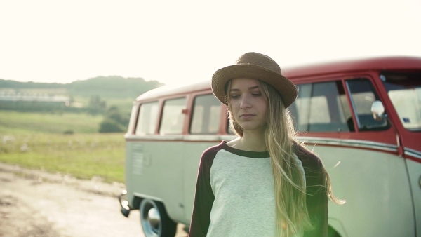 A young sad girl on a roadtrip through countryside, standing by a minivan. Slow motion.