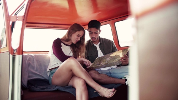 A young couple on a roadtrip through countryside, sitting in retro minivan and looking at a map. Slow motion.