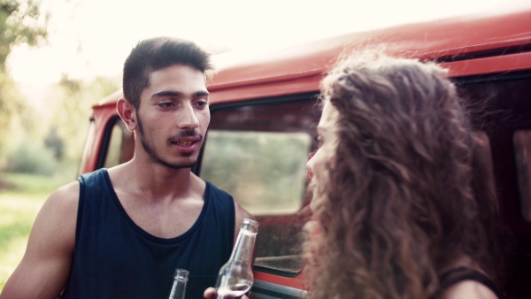 A young couple on a roadtrip through countryside, standing by retro minivan and talking.