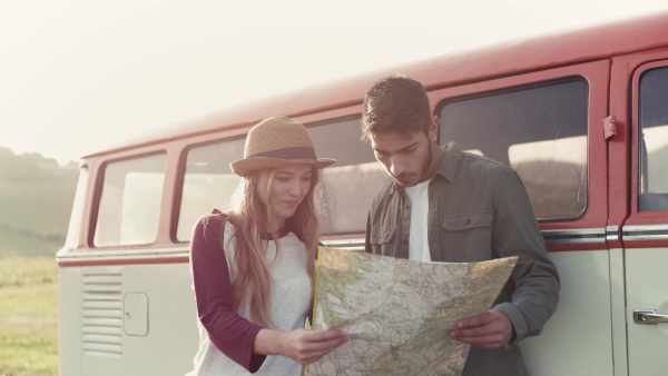 A young couple on a roadtrip through countryside, sitting in retro minivan and looking at a map.