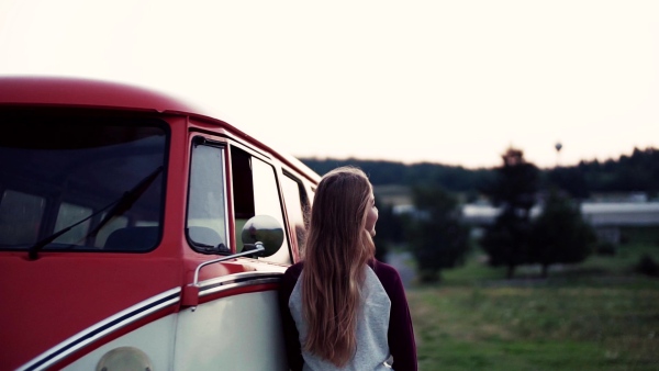 A young girl stabding by a car on a roadtrip through countryside. Slow motion.