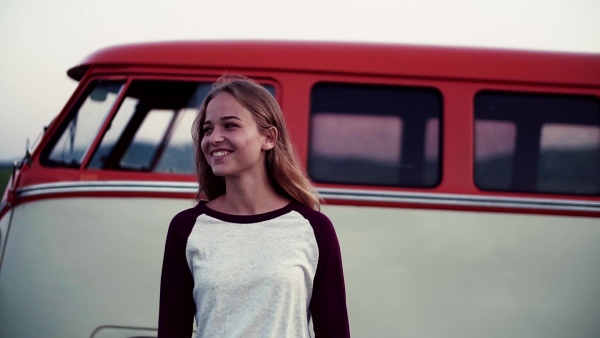 A young happy girl on a roadtrip through countryside, standing by a minivan. Slow motion.