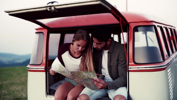 A young couple on a roadtrip through countryside, sitting in retro minivan and looking at a map. Slow motion.