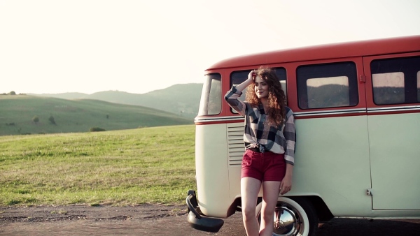 A young girl stabding by a car on a roadtrip through countryside. Slow motion.