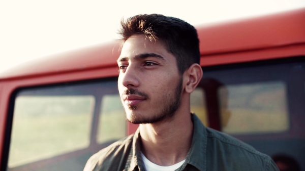 A young happy boy on a roadtrip through countryside, standing by a minivan. Slow motion.