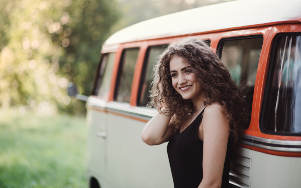 A young girl on a roadtrip through countryside, standing by a minivan. Copy space.