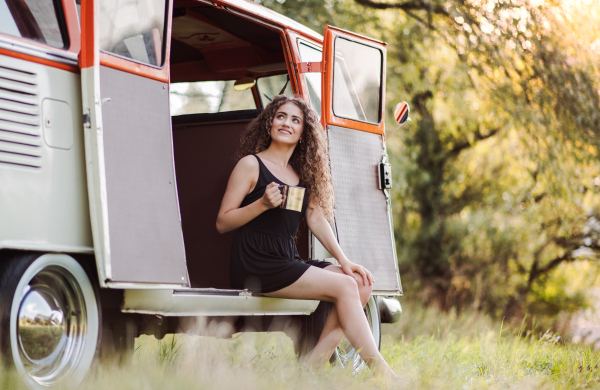 A cheerful young girl sitting in the boot of a car on a roadtrip through countryside.