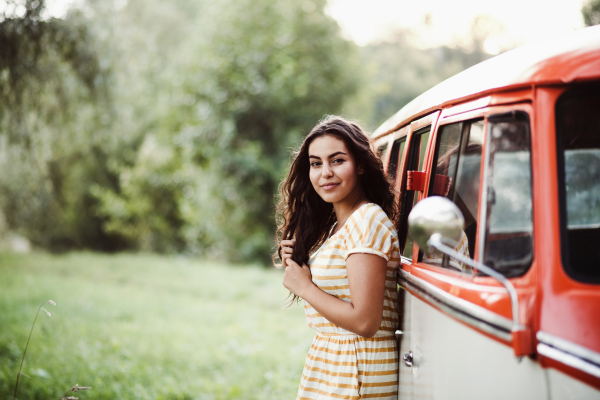 A cheerful young girl standing by a car on a roadtrip through countryside.