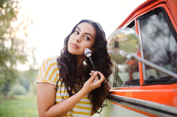 A young girl looking in mirror and applying makeup on a roadtrip through countryside.