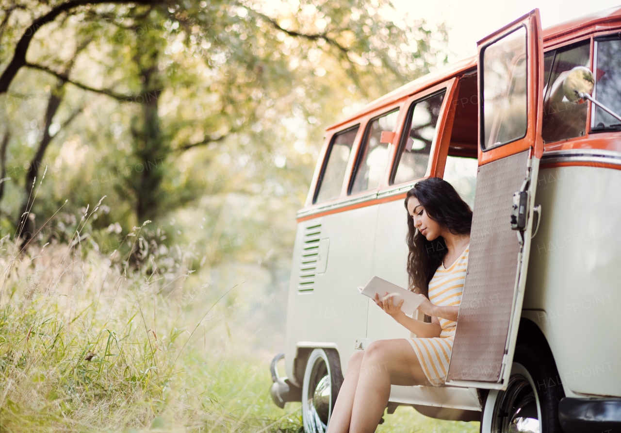 A cheerful young girl with book by a car on a roadtrip through countryside, reading. Copy space.