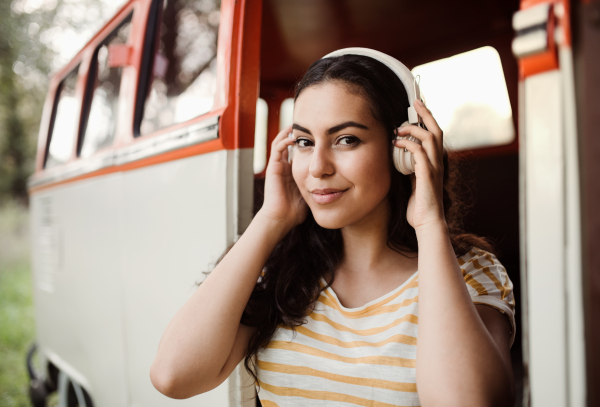 A young girl with headphones by a car on a roadtrip through countryside, listening to music.