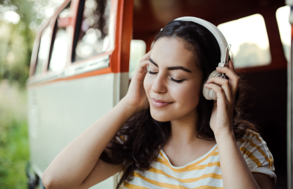 A young girl with headphones by a car on a roadtrip through countryside, listening to music.