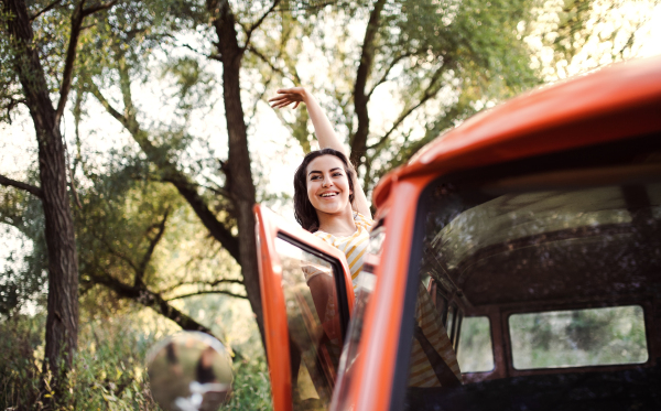 A cheerful young girl on a roadtrip through countryside, waving at somebody from a car.