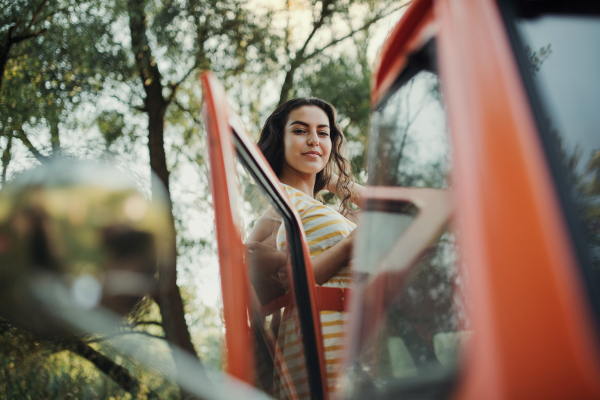 A beautiful young girl standing by a car on a roadtrip through countryside.