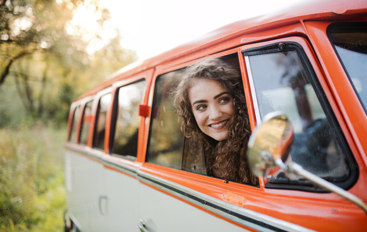 A cheerful young girl looking out of a car on a roadtrip through countryside.