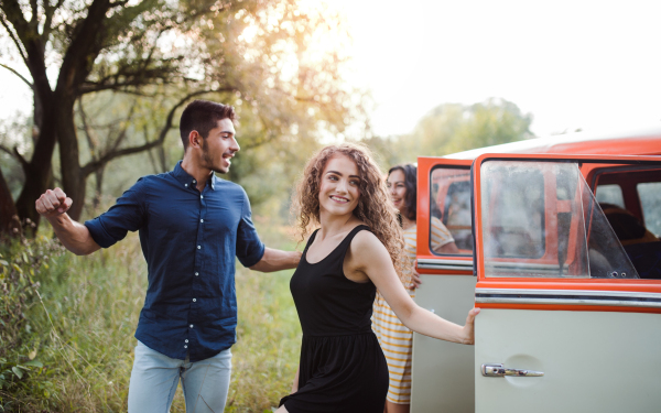 A group of young friends standing by a retro minivan on a roadtrip through countryside.