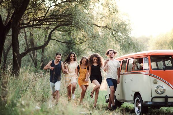 A group of young friends walking by a retro minivan on a roadtrip through countryside.