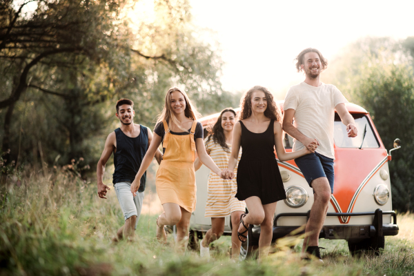 A group of young friends walking in front of a retro minivan on a roadtrip through countryside, running.