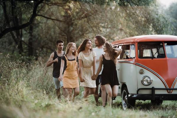 A group of young friends walking by a retro minivan on a roadtrip through countryside.