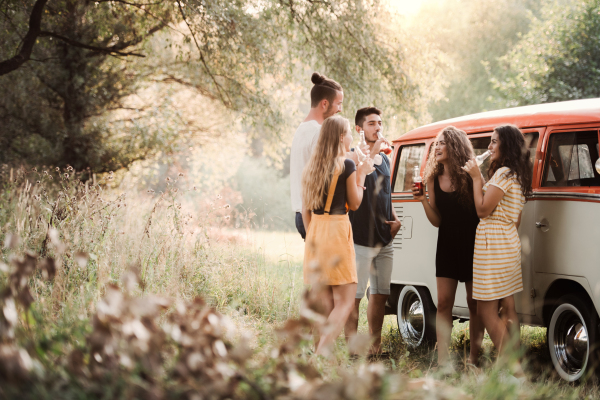 A group of young friends with drinks standing outdoors on a roadtrip through countryside, drinking from bottles.