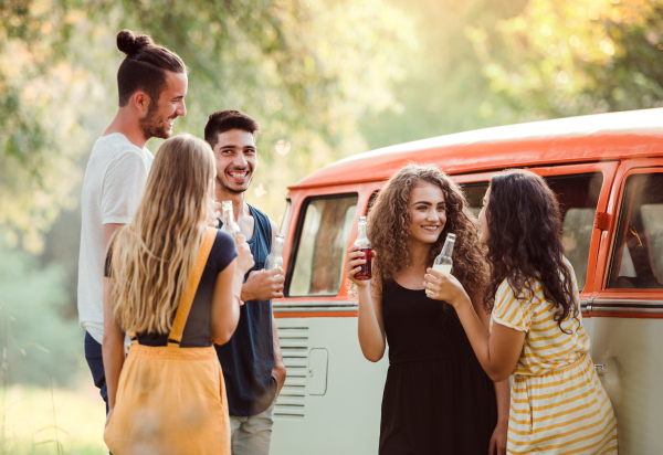 A group of young friends with drinks standing outdoors on a roadtrip through countryside, holding bottles.